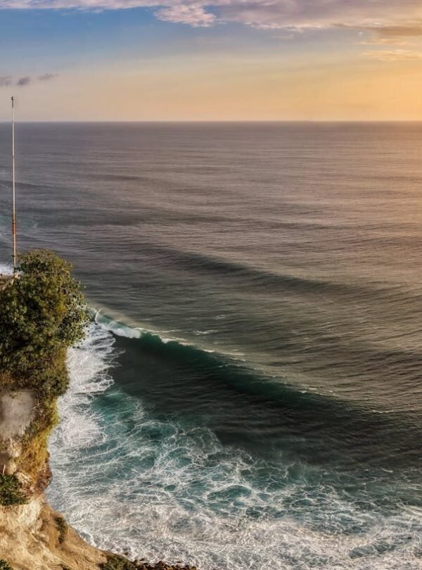 A breathtaking aerial view of Uluwatu Temple perched on cliffs overlooking the ocean at sunset in Bali, Indonesia.