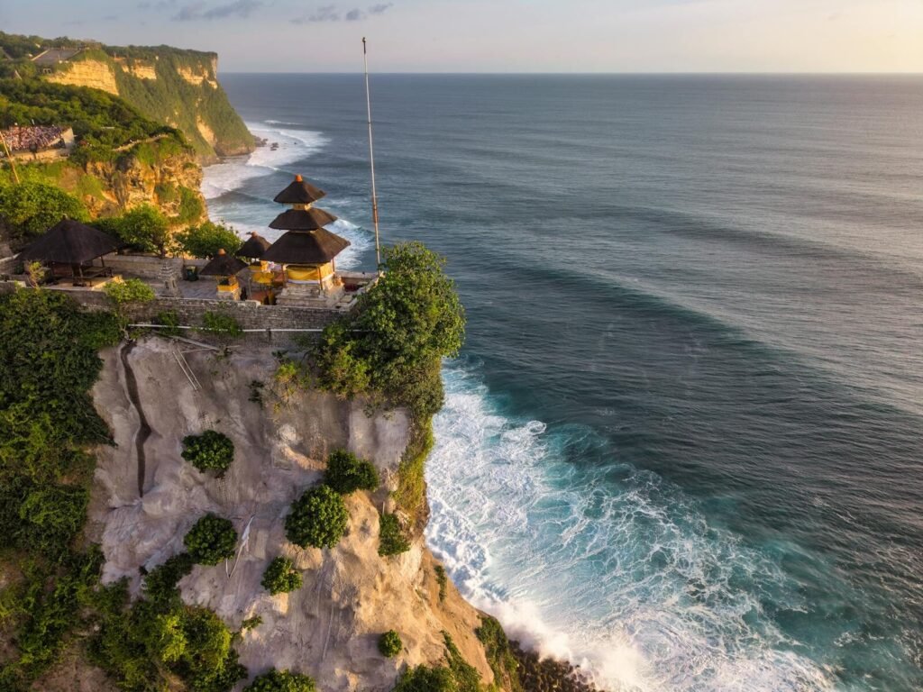 Aerial view of Uluwatu Temple perched on a cliff in Bali, Indonesia, at sunset.