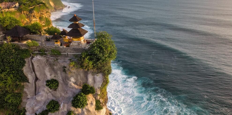 Aerial view of Uluwatu Temple perched on a cliff in Bali, Indonesia, at sunset.